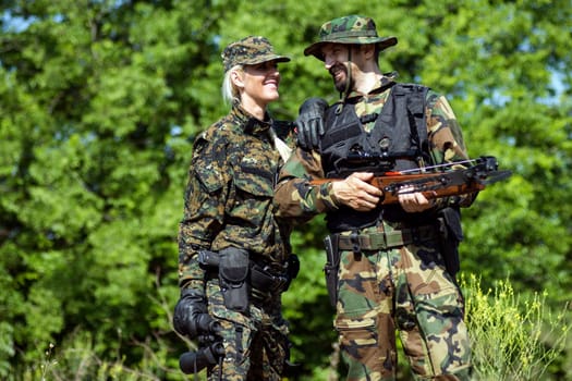 The female and male army soldiers are in different military uniforms outdoors in nature on green background.