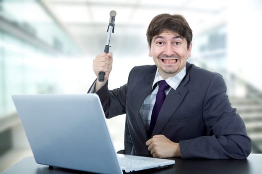 young crazy business man with a hammer smashing a laptop
