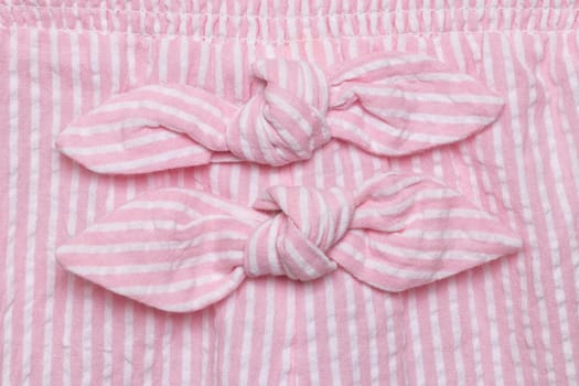 Bow on dress. Close-up details of two decoration ties at pink white striped summer dress of little girl. Macro.