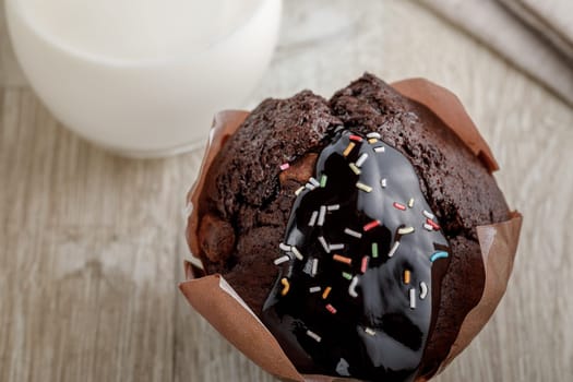 Chocolate cake in baking paper on a wooden surface, and with chocolate icing and decorative powder
