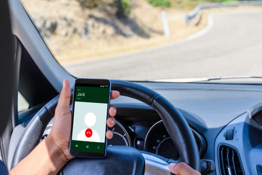 Young driver, using smartphone, on the road in the car. Distraction and danger on the road.