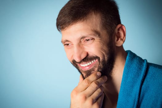 Beauty portrait of smiling handsome middle aged bearded man on blue background, cosmetics for men and male beauty concept.