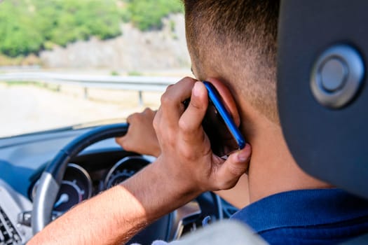 Young driver, using smartphone, on the road in the car. Distraction and danger on the road.