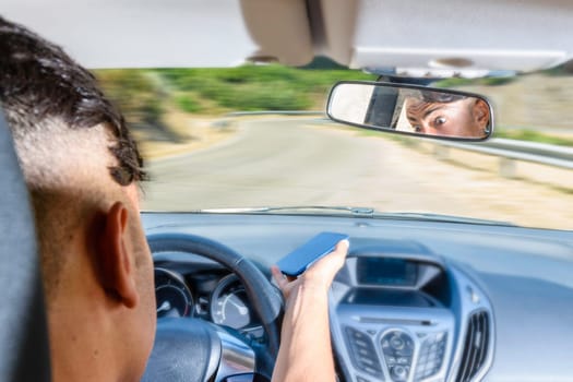 Young driver, using smartphone, on the road in the car. Distraction and danger on the road.