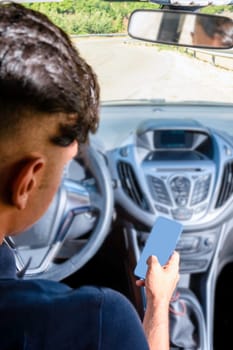 Young driver, using smartphone, on the road in the car. Distraction and danger on the road.