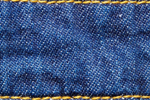 Denim background texture. Close-up of blue jeans fabric frame with simple yellow seam at the top and bottom. Large copy space for design. Beautiful backdrop. Macro.