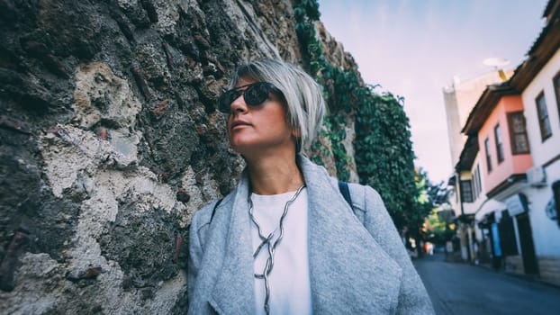 Beautiful blonde adult female standing against wall.