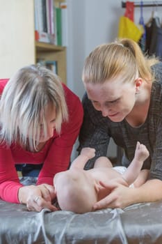 Two women together are playing with little baby lying on the blanket.