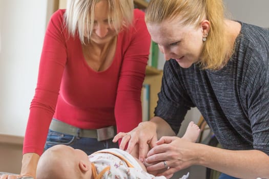 Two smiling women are changing diaper to little baby boy.