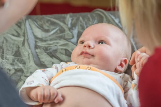 Top view of little baby lying on the blanket and looking at two women bending over him.