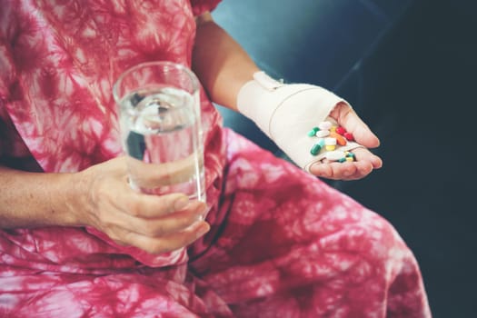 Senior asian woman take pill medicine on hand while sitting on sofa at home