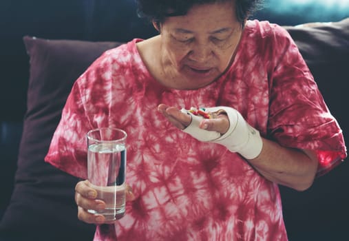Senior asian woman take pill medicine on hand while sitting on sofa at home
