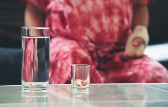 Senior asian woman take pill medicine on hand while sitting on sofa at home