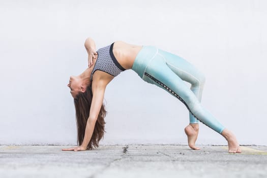 Fit sporty active girl in fashion sportswear doing yoga fitness exercise in front of gray wall, outdoor sports, urban style.