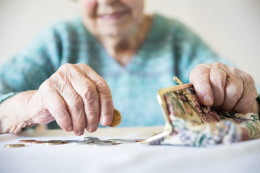 Detailed closeup photo of elderly 96 years old womans hands counting remaining coins from pension in her wallet after paying bills. Unsustainability of social transfers and pension system.