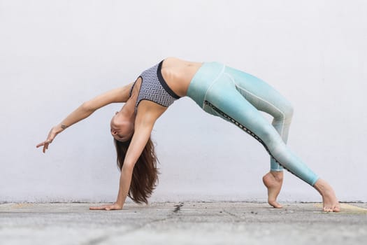 Fit sporty active girl in fashion sportswear doing yoga fitness exercise in front of gray wall, outdoor sports, urban style.