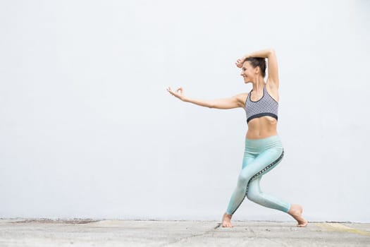 Fit sporty active girl in fashion sportswear doing yoga fitness exercise in front of gray wall, outdoor sports, urban style.