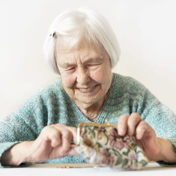Cheerful elderly 96 years old woman sitting at table at home happy with her pension savings in her wallet after paying bills. Saving for retirement and financial planing concept.