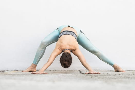 Fit sporty active girl in fashion sportswear doing yoga fitness exercise in front of gray wall, outdoor sports, urban style.