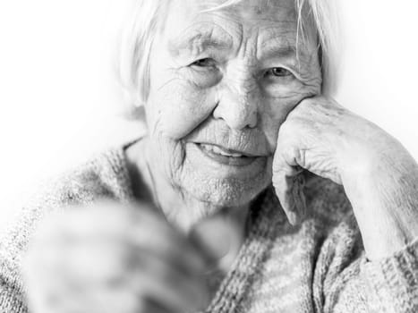Cheerful elderly 96 years old woman sitting at table at home happy with a coin in her hand. Saving for retirement and financial planing concept. Black and white image.