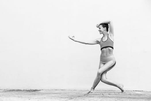 Fit sporty active girl in fashion sportswear doing yoga fitness exercise in front of gray wall, outdoor sports, urban style. Black and white image.