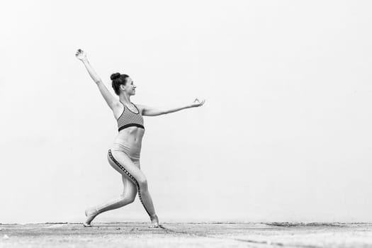 Fit sporty active girl in fashion sportswear doing yoga fitness exercise in front of gray wall, outdoor sports, urban style. Black and white image.