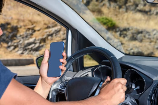 Young driver, using smartphone, on the road in the car. Distraction and danger on the road.