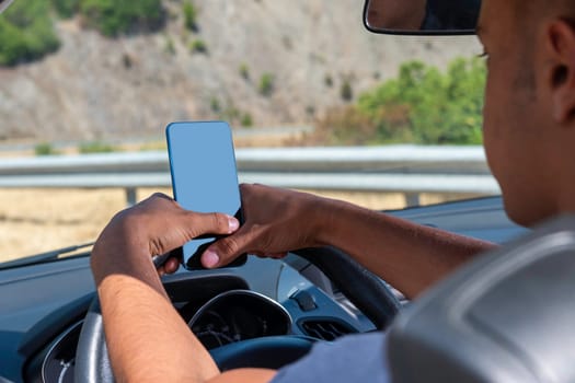 Young driver, using smartphone, on the road in the car. Distraction and danger on the road.