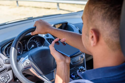Young driver, using smartphone, on the road in the car. Distraction and danger on the road.