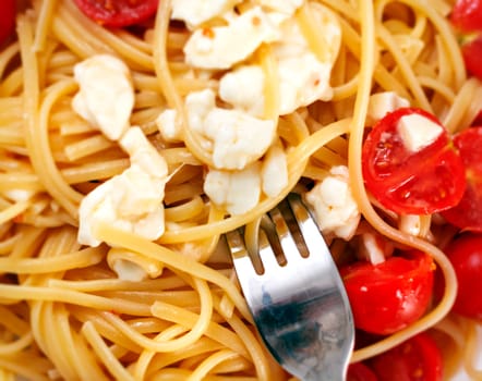 Top view of a plate of spaghetti seasoned with cherry tomatoes and fresh mozzarella with a fork ready to roll them. Italian food and cuisine. Cooked food