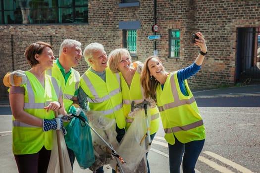 A group of five people taking a selfie. They are wearing high visibility jackets and are participating in a city clean-up.