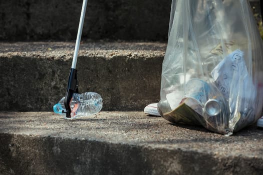 A close-up of an unrecognizable person picking up a plastic bottle on the streets.