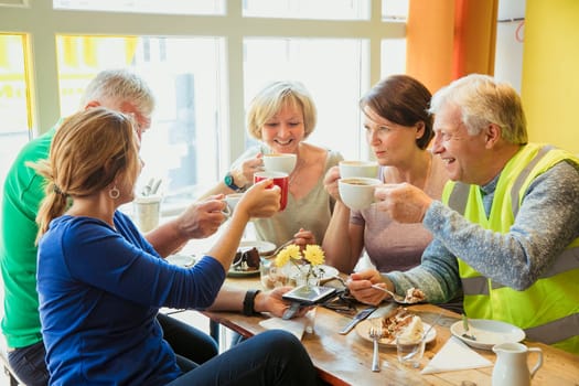 A group of five people taking a break from city cleaning and having coffee and cake.