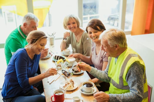A group of five people taking a break from city cleaning and having coffee and cake.