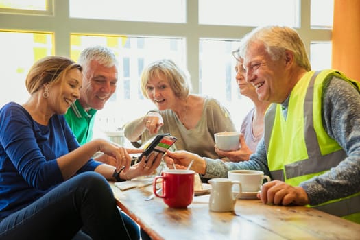 A group of five people taking a break from city cleaning and having coffee and cake they are looking at one of their phones.