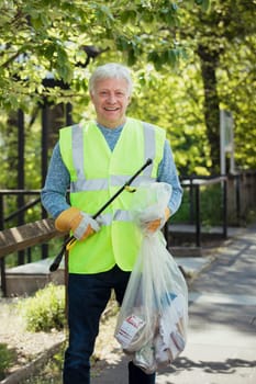 A portrait of a mature man standing in a park, wearing. a high visibility jacket and participating in a city clean up.
