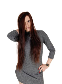 A beautiful slim young woman standing with her long brunette hair.and gray dress, looking serious, isolated for white background.