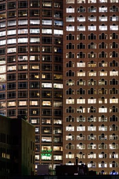 Late Working urban concept, window facade of business center office building at night, Boston, MA, USA.