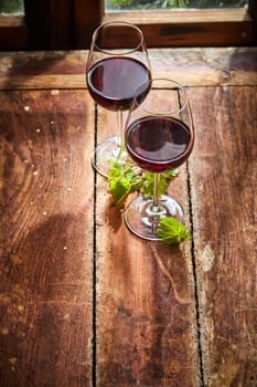 Two glasses of red wine with fresh young green vine leaves on an old rustic wooden table in front of a window in a high angle view with copy space