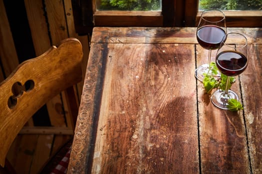 Two glasses of red wine served on a rustic old table with copy space for product or food placement in light from a window
