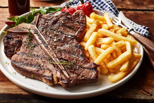 Tasty grilled T-bone steak seasoned with herbs and spices served with deep fried potato chips and salad in a close up view for menu advertising