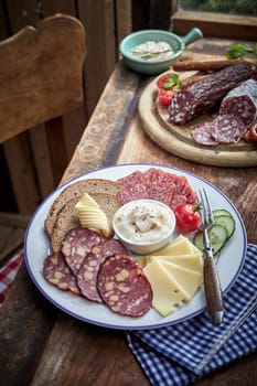Plate of sliced wild venison sausage and cheese served with a dip and rye bread for a tasty lunch in a rustic tavern or pub