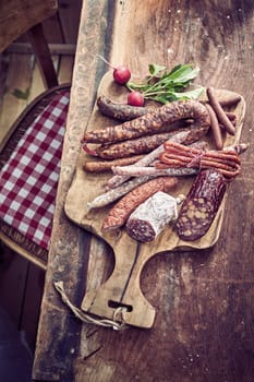 Variety of different wild venison dried sausages on a board with fresh radish served on a rustic old table in a high angle view
