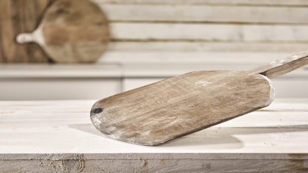 Old empty floured wooden pizza paddle on a rustic white kitchen table with copy space for food or product placement