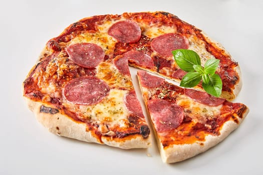 Sliced Italian salami pizza garnished with fresh basil over a white background for advertising or a menu