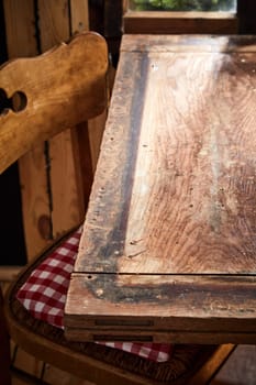 Old rustic bare empty table and chair in front of a window in a tavern or pub with copy space for product or food placement in vertical format