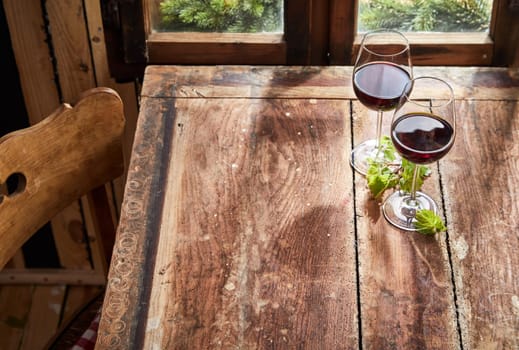 Two glasses of red wine with fresh green leaves standing on an old rustic table in front of a window with copy space in a high angle view