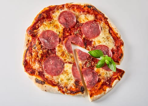 Sliced pepperoni pizza with fresh basil leaves, melted mozzarella and tomato paste seasoned with herbs viewed from above isolated on white