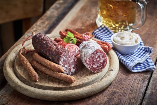 Wooden board with assorted spicy wild venison sausages served with a dip or dressing and mug of beer on an old rustic wooden table