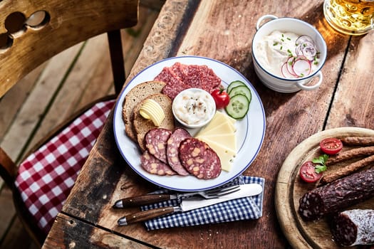 Buffet selection of venison sausages on a wooden board with lunch platter of sliced meat and cheese served with rye bread and salad sides and a mug of beer